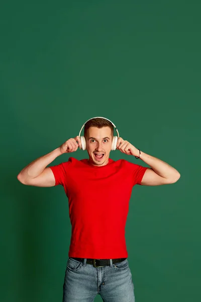 緑の背景の上に隔離された楽しい顔を持つヘッドフォンでポーズカジュアルな服の若い男の肖像画 ライフスタイル カジュアルなファッション 表情の概念 — ストック写真