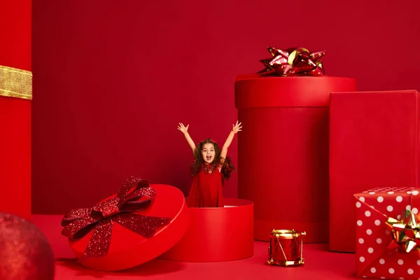 赤い背景の上に現在の箱から現れる美しいドレスの子供 幸せなかわいい女の子 メリークリスマス お祝い プレゼント 買い物や販売の概念です 広告のコピースペース — ストック写真