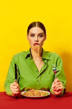 Spagetti yiyen genç bir kız, sarı arka planda ağzında erişteler var. Yemek vakti. Duygusuz, poker suratlı. Yemek ve sanat fotoğrafçılığı. Tamamlayıcı renkler. İlan, metin için boşluk kopyala