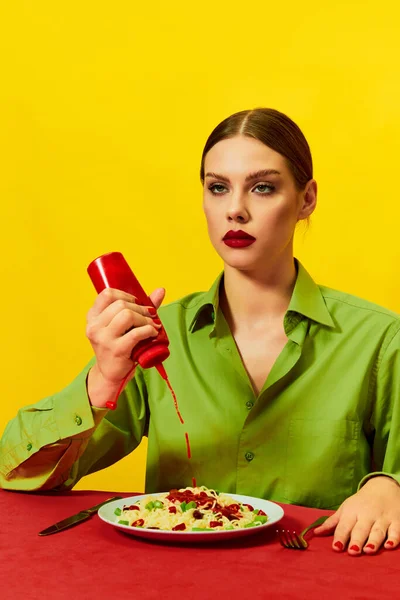 年轻姑娘 无表情的脸把番茄酱倒在盘子里 红桌布上的意大利面撒在黄色的背景上 食品流行艺术摄影 互补的颜色 文字的复制空间 — 图库照片