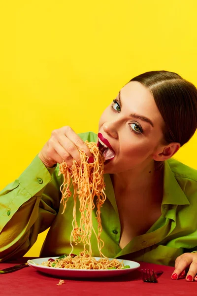 多愁善感的小女孩吃着意大利面 手放在红色桌布上抹在黄色背景上的面条 饿了食品流行艺术摄影 互补的颜色 复制空间为广告 — 图库照片