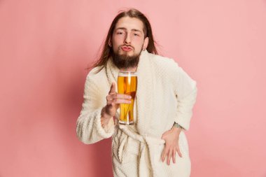 Partiden sonra. Bornozlu komik adam pembe arka planda izole edilmiş bir bardak bira ile duygusal poz veriyor. İçecek bir şeyler. Duyguların kavramı, zevk, yaşam tarzı, yüz ifadesi, Ekim Festivali