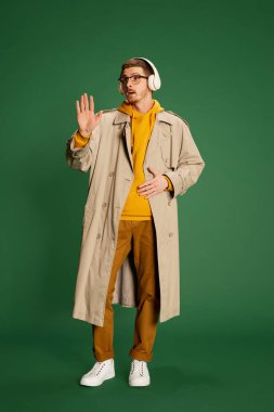 Yeşil arka planda izole edilmiş kulaklıkla poz veren modaya uygun giyinmiş genç bir adamın portresi. Dikkat! Gençlik kavramı, yaşam tarzı, gündelik moda, duygular, yüz ifadesi. Ad