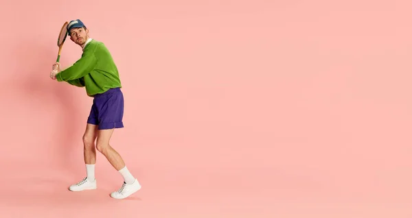 Portrait of young man in vintage sportive clothes posing with tennis racket isolated on pink background. Flyer. Concept of retro fashion, sport, 90s, lifestyle, youth, emotions. facial expression. Ad