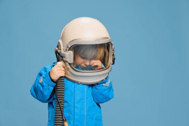 Küçük bir çocuğun portresi, astronot kostümü giymiş çocuk, mavi stüdyo arka planında ağlıyor. Gözyaşlarını siliyorum. Çocukluk kavramı, duygular, yaşam tarzı, moda, mutluluk. İlan için alanı kopyala
