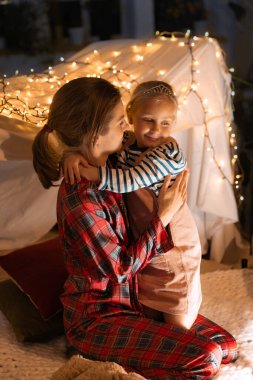 Anne, küçük kızıyla vakit geçirir, kendi kendine kulübede oynar, akşamları odada çadır kurar. Rahatlık ve rahatlık. Fantezi, çocukluk, aile, boş zaman, aşk, bakım, ev.