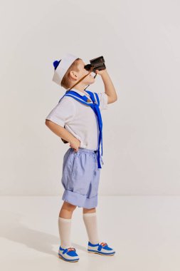 Küçük bir çocuğun portresi, yelek giymiş gri arka planda dürbünle poz veren bir çocuk. Yaz tatili. Çocukluk kavramı, arkadaşlık, eğlence, yaşam tarzı, moda, seyahat, duygular