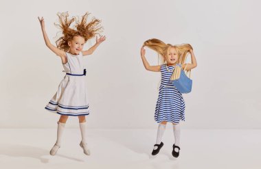 İki küçük kızın portresi, şirin elbiseli çocuklar poz veriyor, gri arka planda eğleniyorlar. Çocukluk kavramı, arkadaşlık, eğlence, yaşam tarzı, moda, eski tarz, duygular