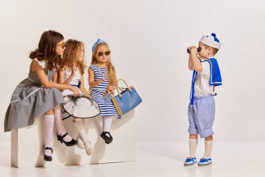 Gri arka planda poz veren çocukların portresi. Oğlan üç kızın fotoğrafını çekiyor. Seyahat ve hatıralar. Çocukluk kavramı, arkadaşlık, eğlence, yaşam tarzı, moda, eski tarz, duygular