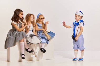 Gri arka planda poz veren çocukların portresi. Yolculukta kızlarla tanışan bir çocuk. Tanıdıklar. Çocukluk kavramı, arkadaşlık, eğlence, yaşam tarzı, moda, eski tarz, duygular