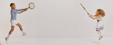 Çocuk portresi, deniz tarzı giyinmiş kız ve erkek badminton oynuyor, gri arka planda poz veriyor. Çocukluk kavramı, arkadaşlık, eğlence, yaşam tarzı, moda, eski tarz, duygular