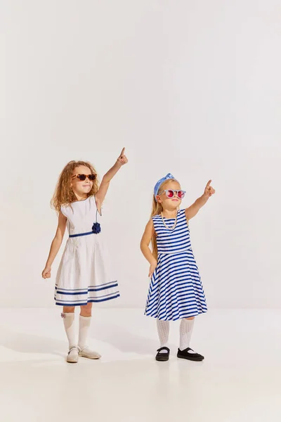 Portret Dwóch Dziewczynek Dzieci Uroczych Sukienkach Okularach Przeciwsłonecznych Wskazujący Szare — Zdjęcie stockowe