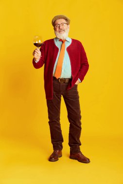 Klasik elbiseli, gözlüklü ve şapkalı son sınıf öğrencisinin portresi kırmızı şarapla canlı sarı arka planda poz veriyor. Degukasyon. Duyguların kavramı, yüz ifadesi, yaşam tarzı, modern moda.