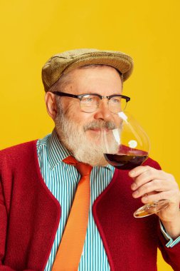 Klasik giyinmiş, gözlüklü ve şapkalı son sınıf öğrencisinin portresi, canlı sarı arka planda kırmızı şarap kokusu. Degukasyon. Duyguların kavramı, yüz ifadesi, yaşam tarzı, modern moda.