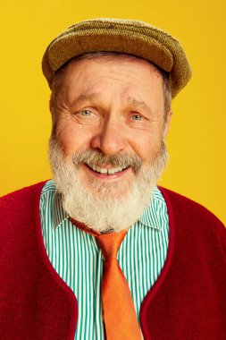 Klasik giyinmiş, gözlüklü, şapkalı, parlak sarı arka planda gülümseyen son sınıf öğrencisinin portresi. Yumuşak başlı bir adam. Duyguların kavramı, yüz ifadesi, yaşam tarzı, modern moda.