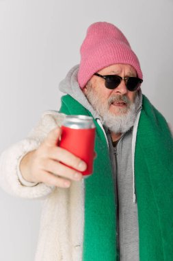 Şık bir son sınıf öğrencisinin portresi, örgü ören pembe şapkalı yaşlı bir adam ve gri arka planda poz veren yeşil bir eşarp. Moda, modern görünüş. Duyguların kavramı, yüz ifadesi, yaşam tarzı, modern moda.