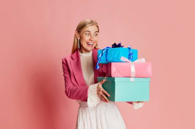 Güzel, şık bir kadının portresi pembe arka planda mevcut kutularla duygusal poz veriyor. Kutlama, parti, kadınlar günü, duygular, bayram, doğum günü, mutluluk kavramı. Ad