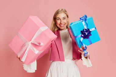 Güzel, şık bir kadının portresi pembe arka planda mevcut kutularla duygusal poz veriyor. İyi tatiller. Kutlama, parti, kadınlar günü, duygular, bayram, doğum günü, mutluluk kavramı. Ad