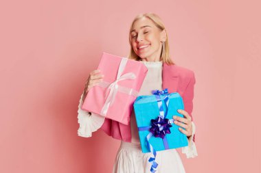 Güzel, şık bir kadının portresi pembe arka planda mevcut kutularla duygusal poz veriyor. Kutlama, parti, kadınlar günü, duygular, bayram, doğum günü, mutluluk kavramı. Ad