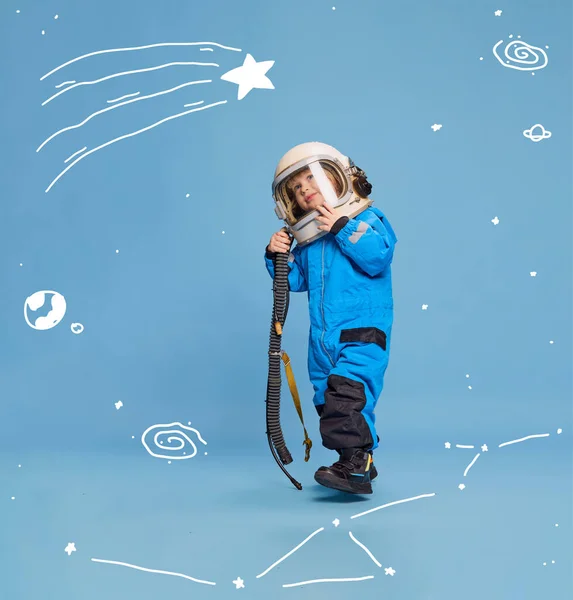 Creative design with drawn elements. Portrait of little boy, child in costume of astronaut over blue background. Playful kid. Concept of imagination, childhood, creativity, dreams, ad