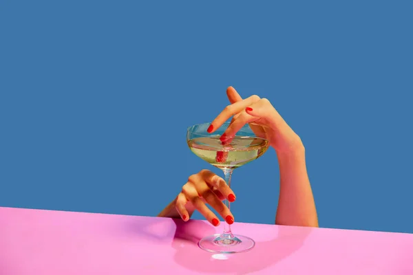 Female hands holding glass with champagne over blue pink background. Celebration. Concept of holiday, party, drink. Complementary colors. Copy space for ad. Pop art. Copy space for ad