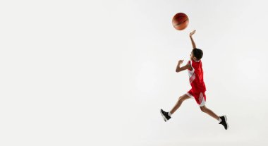 Kırmızı üniformalı bir çocuğun portresi, gri stüdyo arka planında basketbol oynuyor. Pankart. Enerji kavramı, profesyonel spor, hareket, eylem, hobi, rekabet, başarı.