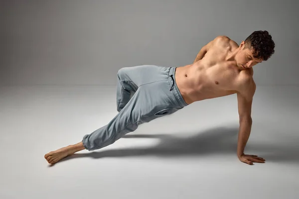 Mature man posing shirtless, in pants over grey studio background. Fit, strong, muscular body shape. Attraction. Concept of mens health and beauty, body and skin care, fitness. Body art