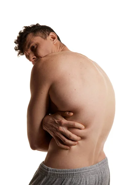Round back. Healthy, strong back, spine. Man posing shirtless, in pants over white studio background. Muscular body. Concept of mens health and beauty, body and skin care, fitness. Body art