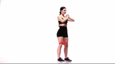 Genç, sportif kız, beyaz stüdyo geçmişi üzerinden antrenman yapıyor. Fitness elastik bantlarla çömelmek. Bacak ve kalça egzersizi. Spor, aksiyon, hareket, gençlik kavramı. Fitness, hobi, sağlıklı yaşam tarzı