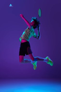Üniformalı, badminton oynayan genç bir çocuk neon ligth 'te mavi mor arka planda mekik penisine çarpıyor. Spor yaşam tarzı kavramı, hareket, eylem, rekabet