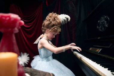 Şirin küçük bir kızın portresi, ortaçağ kraliyet mensubu muhteşem elbiseli bir çocuk piyanonun başında oturuyor ve duygusal olarak çalıyor. Tarihi yeniden yapılanma kavramı, çağların karşılaştırması, ortaçağ modası