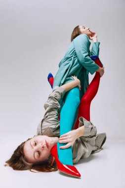Olağanüstü bir davranış. Gri stüdyo arka planında poz veren parlak kırmızı taytlı ve ceketli iki genç kızın portresi. Modern moda kavramı, queer, sanat fotoğrafçılığı, garip insanlar, yaratıcılık