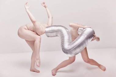 Kendini ifade etme. Bej renkli stüdyo arka planında çıplak iç çamaşırlarıyla poz veren iki genç kızla yaratıcı fotoğrafçılık. Çömelme, tuhaflık, sanat fotoğrafçılığı, garip insanlar, yaratıcılık kavramı.