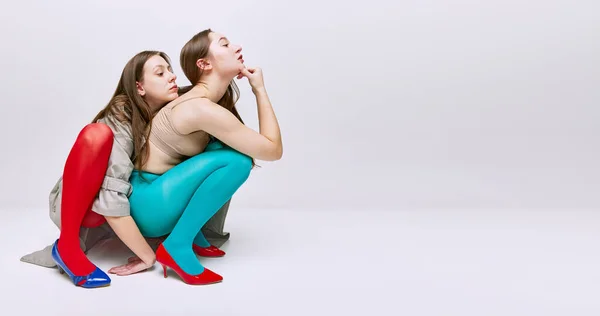 两个穿着鲜红色和蓝色紧身衣 披着灰色工作室背景外套的年轻女孩的画像 班纳现代时尚的概念 艺术摄影 怪异的人 创造力 — 图库照片