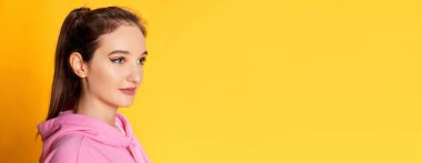 Sarı stüdyo arka planında pembe kapüşonlu güzel bir kızın portresi. Pankart, broşür. Gençlik kavramı, güzellik, moda, yaşam tarzı, duygular, yüz ifadesi. Ad