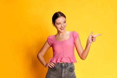 Pozitiflik yayılıyor. Sarı stüdyo arka planında pembe bluzla poz veren güzel bir kızın portresi. Gençlik kavramı, güzellik, moda, yaşam tarzı, duygular, yüz ifadesi. Ad