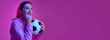 Gergin duygular. Futbol topu arka planında neon ışıkta poz veren duygusal genç bir kızın portresi. Pankart, broşür. Gençlik kavramı, güzellik, moda, yaşam tarzı, duygular, yüz ifadesi. Ad