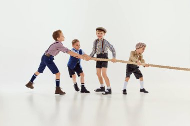 Sportif bir oyun. Bir grup küçük çocuk, birlikte oynayan çocuklar, gri stüdyo arka planında ipi çekiyorlar. Oyun konsepti, çocukluk, arkadaşlık, etkinlik, boş zaman, eski tarz, moda.