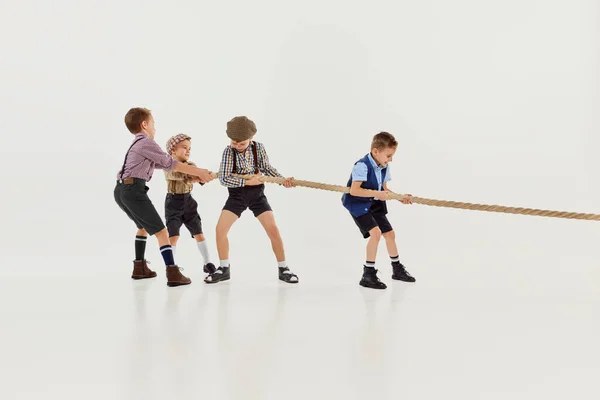 Motivation to win. Group of little boys, children playing together, pulling the rope over grey studio background. Concept of game, childhood, friendship, activity, leisure time, retro style, fashion.