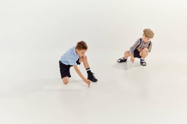 İki çocuk, klasik retro giysili çocuklar yere tebeşirle gri stüdyo arka planlarını çiziyorlar. Oyun konsepti, çocukluk, arkadaşlık, etkinlik, boş zaman, eski tarz, moda.