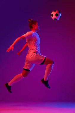Kafasına vur. Genç profesyonel bayan futbol, hareket halindeki futbolcu, antrenman, neon ışıklarıyla oynayan gradyan pembe arka plan. Spor, eylem, hareket, hedefler, rekabet, hobi, reklam kavramı.