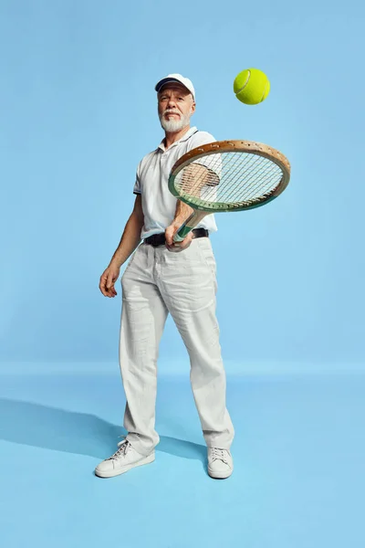 穿着时髦白衣的英俊老年男子的画像 用蓝色背景的网球拍击球球 休闲活动 业余爱好 生活方式 复古风格的概念 — 图库照片