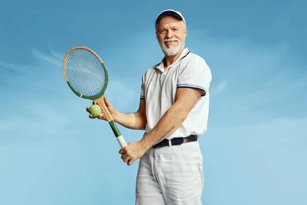 在蓝天背景下 穿着时髦白色服装的英俊老年男子与网球拍合影的肖像 休闲活动 业余爱好 生活方式 复古风格的概念 — 图库照片