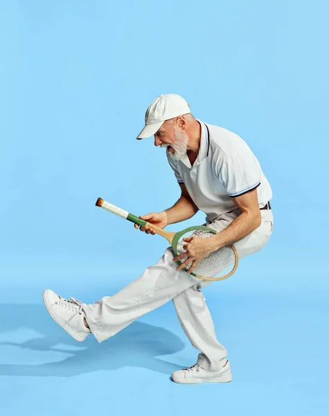 一个穿着时髦的白色服装 穿着蓝色背景网球拍的英俊老年男子的画像 像吉他一样弹奏休闲活动 业余爱好 生活方式 复古风格的概念 — 图库照片