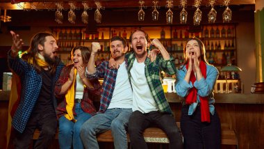 Group of young people, friends, emotionally watching match at pub. Fans cheering up favourite sport team. Winning game. Success. Competition, championship, match translation. Emotions.