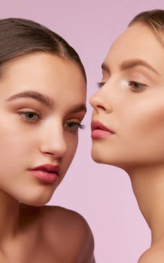 Youth perfection. Portrait of two young, beautiful girls with well-kept skin isolated over pink studio background. Concept of skincare, cosmetology, natural beauty, youth, spa, cosmetics. Ad