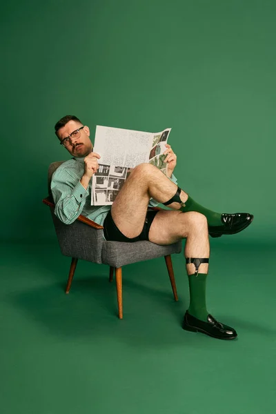 英俊男子的画像 穿着没有裤子的衬衫坐在椅子上 阅读晨报 在绿色工作室的背景下装扮着报纸 面部表情的概念 — 图库照片