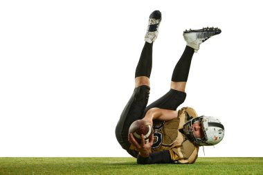 Catching ball and falling. Man, professional american football player in motion, training over white studio background with green grass flooring. Concept of sport, movement, achievements, competition
