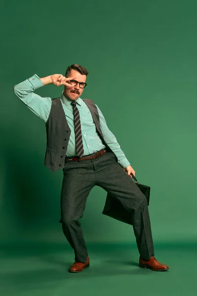 英俊男子的画像 身着古典西装的商人 身披公文包 在绿色工作室的背景上跳舞 庆祝成功 面部表情 时尚的概念 — 图库照片