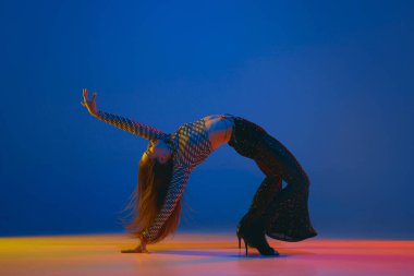Hobby. Portrait of young girl dancing high heel dance in stylish clothes over blue background in neon light. Concept of dance lifestyle, modern style, contemporary, youth culture, self-expression